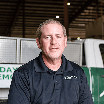Man wearing dark polo shirt with embroidered logo standing in front of shelving and equipment in industrial warehouse setting