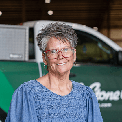 Woman with short gray hair and red glasses smiling at camera, standing in front of a white and green vehicle
