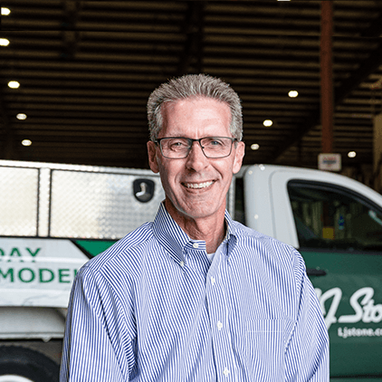 Man with gray hair and glasses wearing a striped shirt, smiling in front of a green and white vehicle in an indoor facility